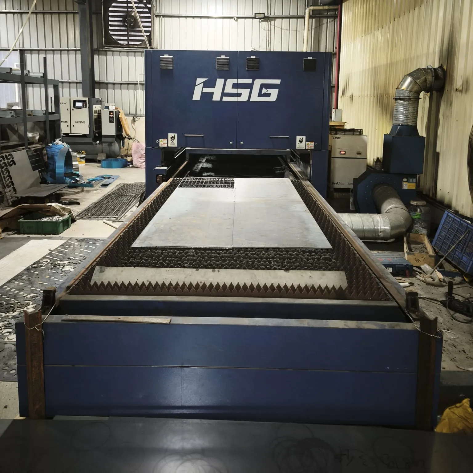 Laser cutting bed with cut steel sheet skeletons beside the machine